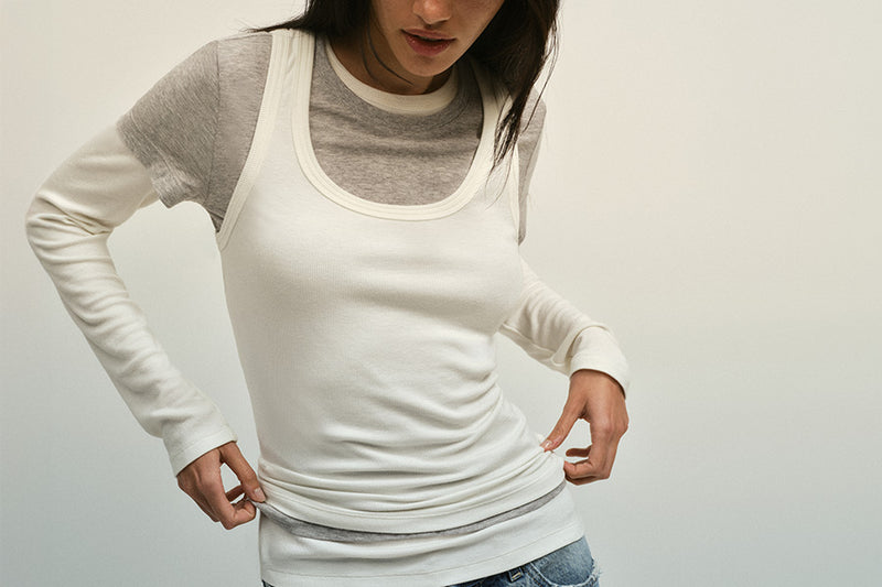 Person wearing a white long-sleeve shirt with gray sleeves on a plain background
