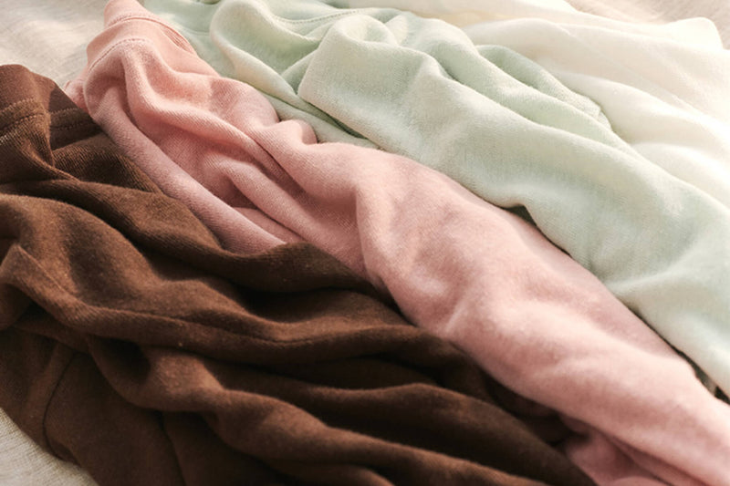A stack of folded fabrics in earthy tones like brown, green, white, and pink.