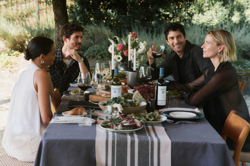 Four people in Summer '26 attire chatting around an outdoor table in a vineyard.
