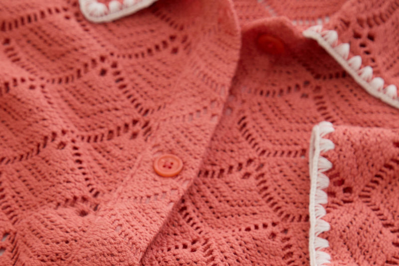 Close-up of coral textured knit fabric with eyelet pattern and button detail.