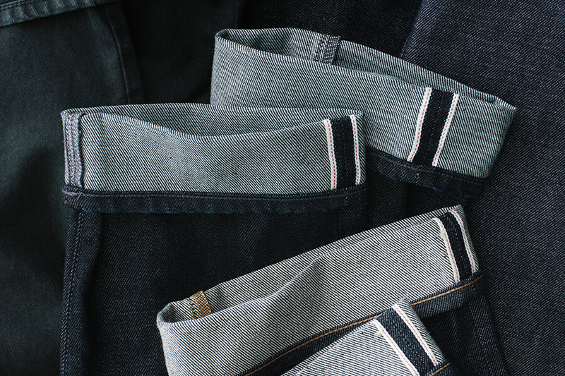 Folded denim jeans with white stitching on a dark background