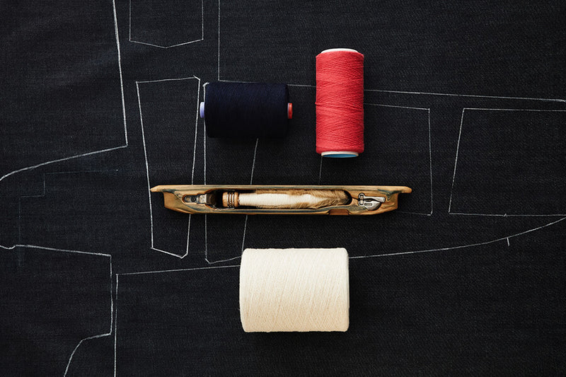 Sewing kit with spools of thread and a needle on a black fabric background