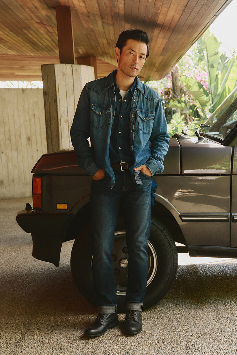 Man in denim shirt and denim blue jeans leaning against car