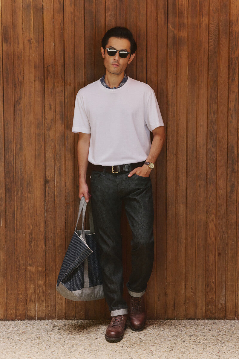 Man in white t-shirt and jeans standing against wall