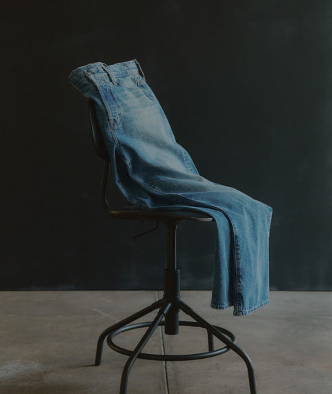 Blue jeans draped over a black stool against a dark background