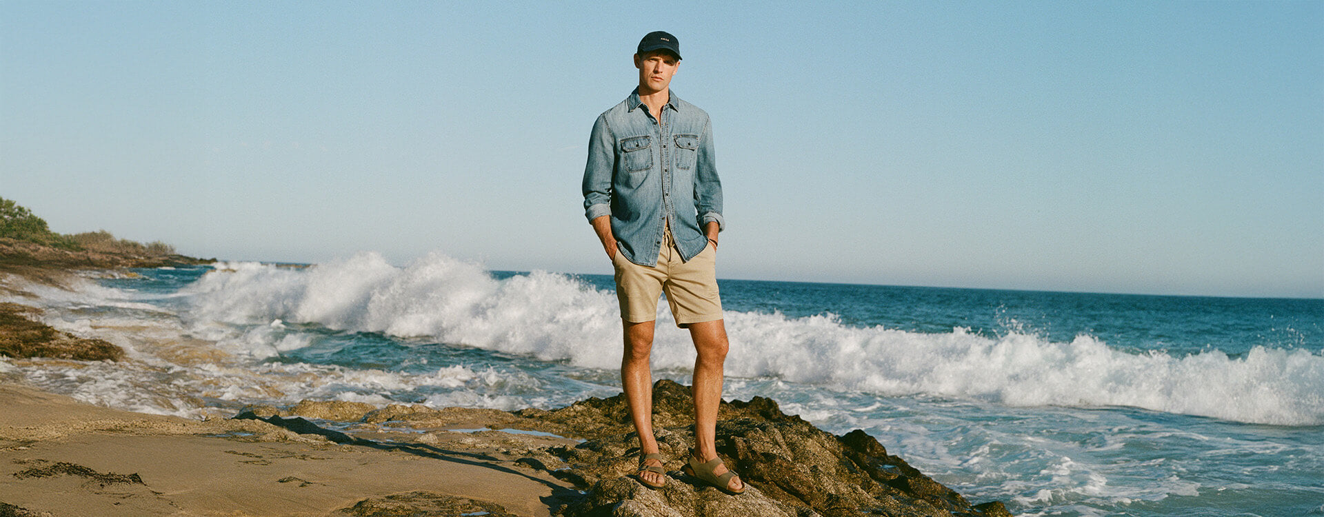 Man in blue shirt and shorts standing next to ocean