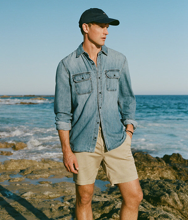 Man in blue shirt and shorts standing next to ocean