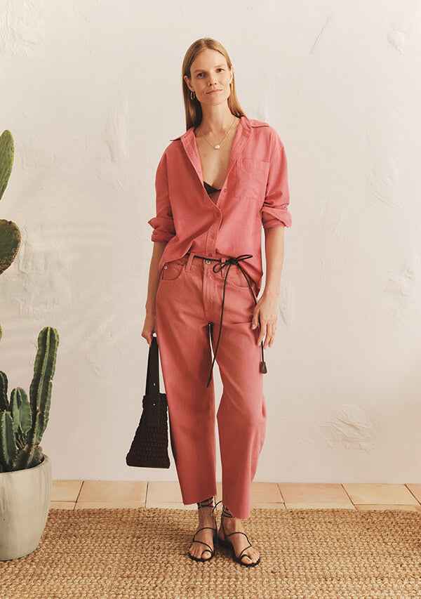 Woman in matching pink shirt and pink jeans carrying a purse in her hand in front of white background