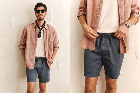 Man with sunglasses, pink shirt, and blue shorts on, standing in front of a white wall