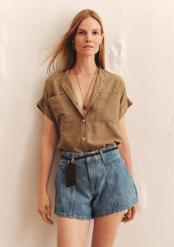 Woman in yellow blouse and blue denim shorts in front of white background