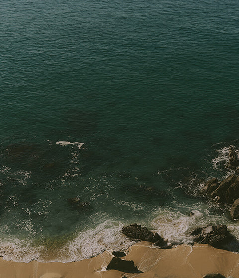 Ocean waves crashing against rocks with a sandy beach.