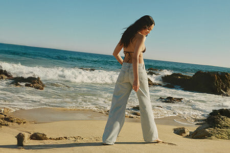 Woman walking on a beach with ocean waves and rocks in the background