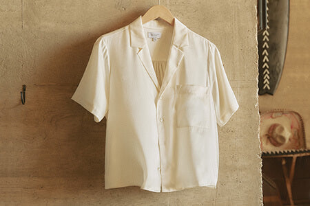 Beige shirt on a hanger against a textured wall.