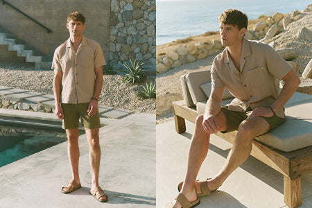 Two men in matching outfits standing by a poolside with a scenic background.