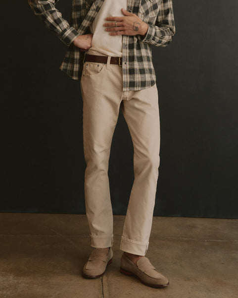 Person wearing a plaid shirt, beige pants, and brown shoes against a dark background