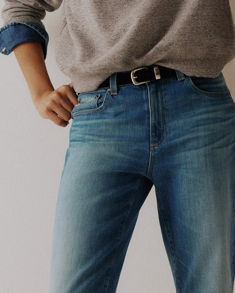 Person wearing blue jeans and a gray sweater on a plain background