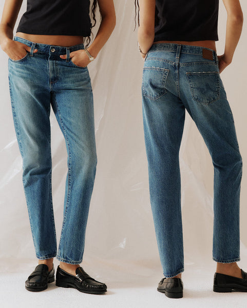Two people wearing blue jeans and black shoes on a plain background