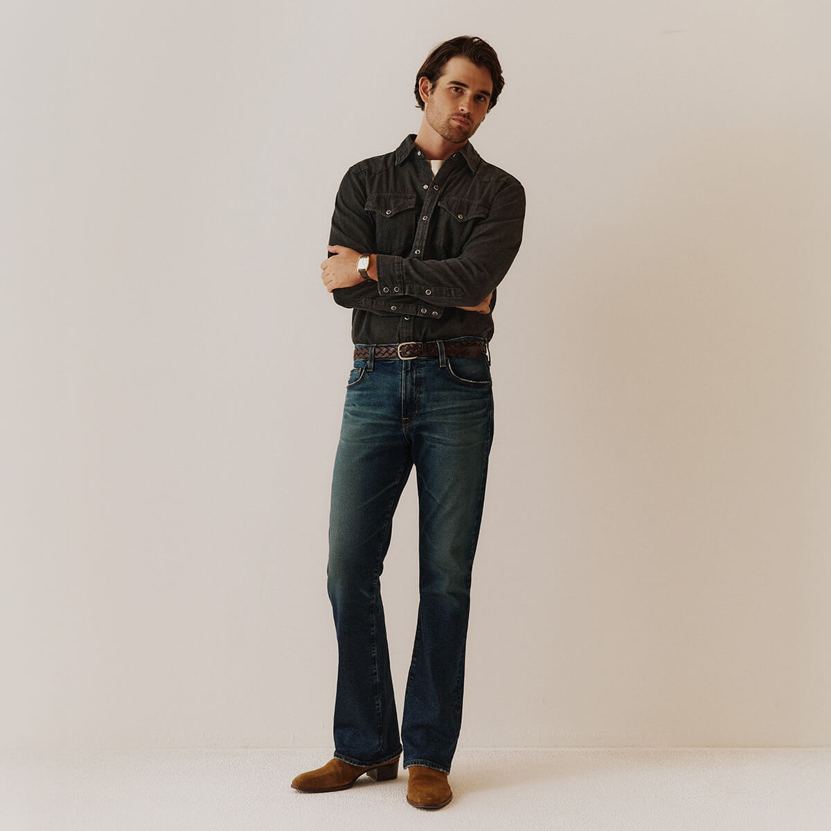 Man wearing a dark denim jacket and jeans standing against a plain background