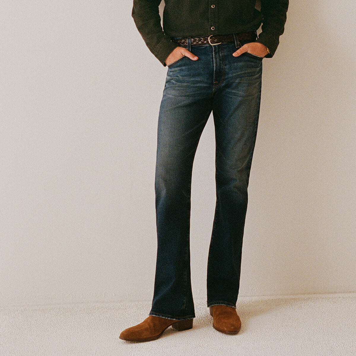 Person wearing blue bootcut jeans and brown shoes on a plain background