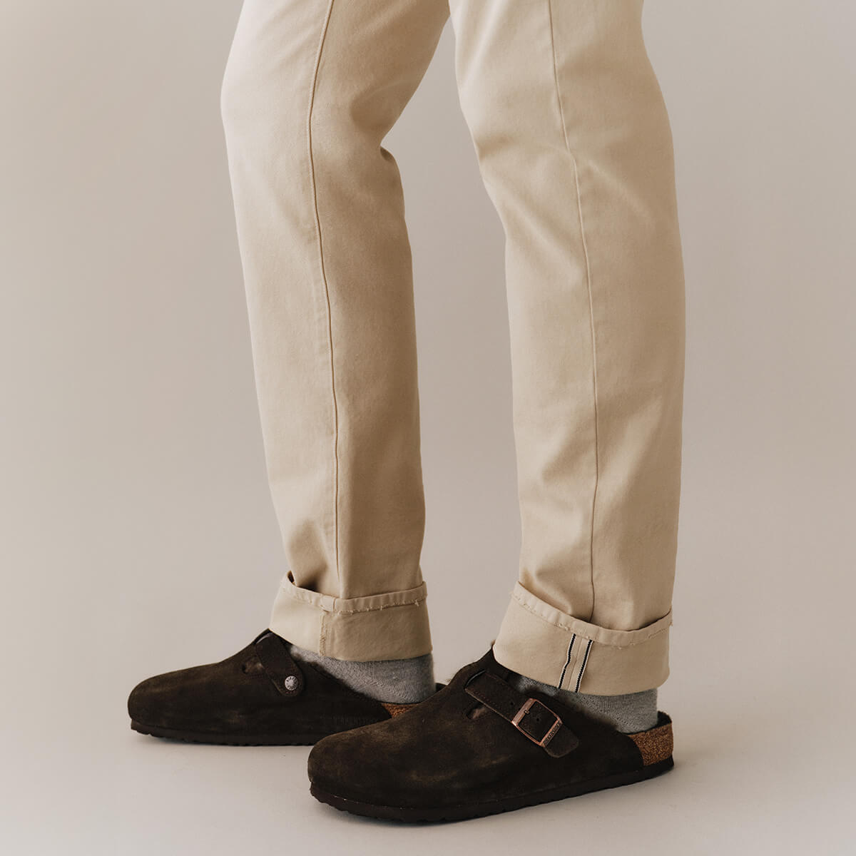 Brown suede shoes worn with beige pants on a neutral background