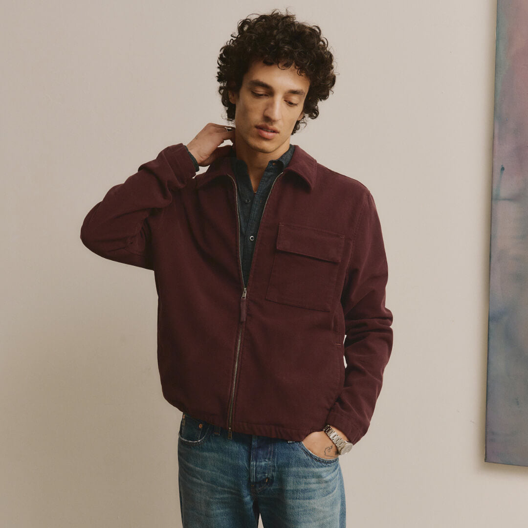 Man wearing a maroon jacket and blue jeans against a neutral background