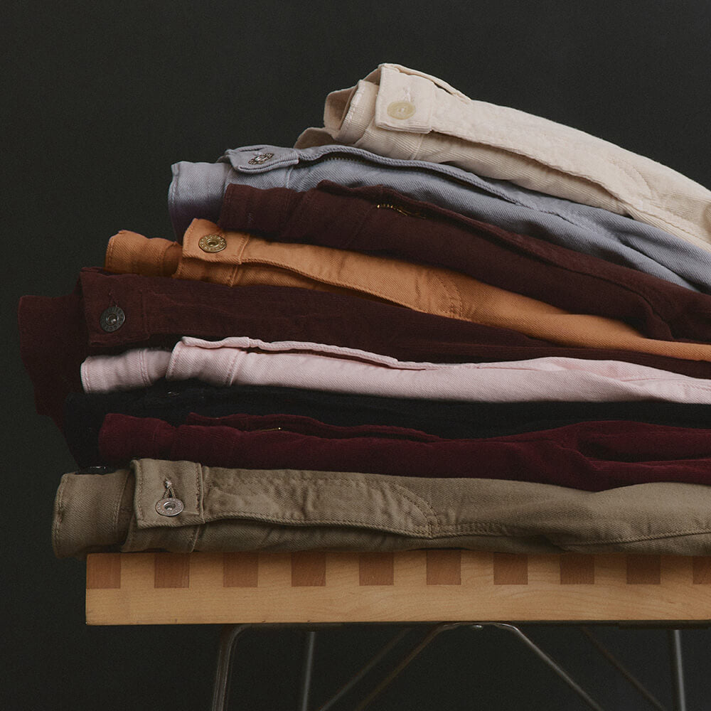 Stack of folded pants on a wooden table with a dark background