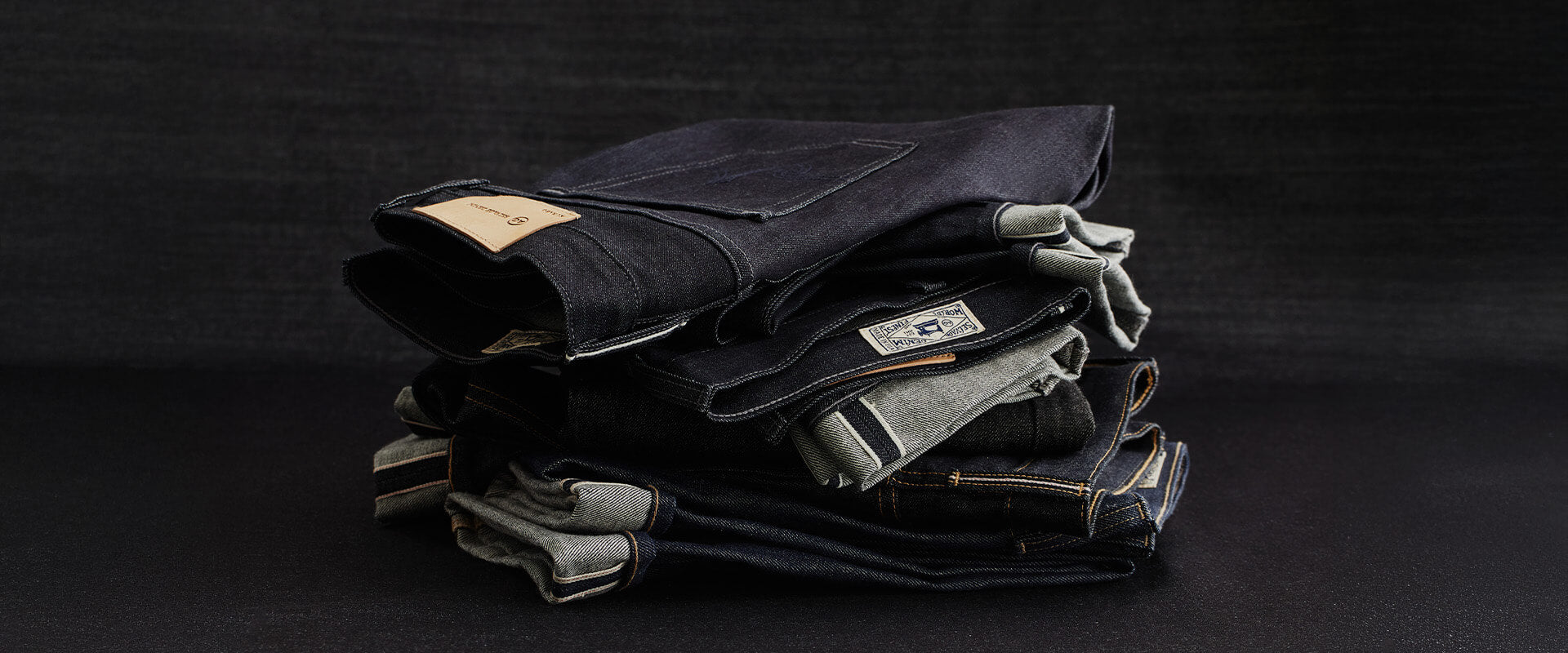 Stack of dark jeans on a black background