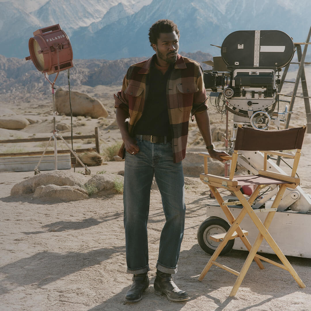 Man standing on a desert film set with movie equipment and mountains in the background
