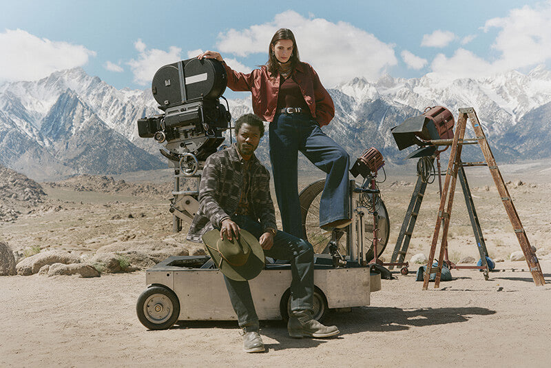 Two people with film equipment in a desert landscape with mountains in the background