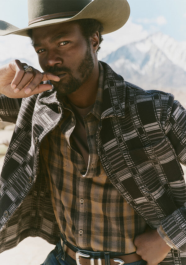 Man wearing a cowboy hat and plaid shirt with mountains in the background
