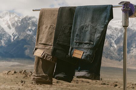 Three pairs of jeans hanging on a clothesline with mountains in the background