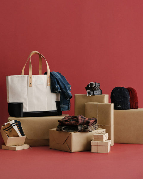 White tote bag with black accents on a red background with boxes and clothing items.