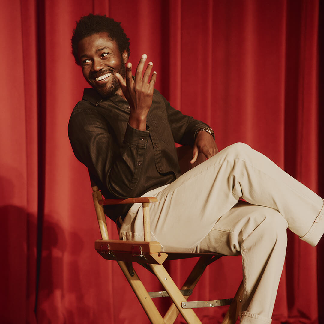 Man sitting on a director's chair against a red curtain