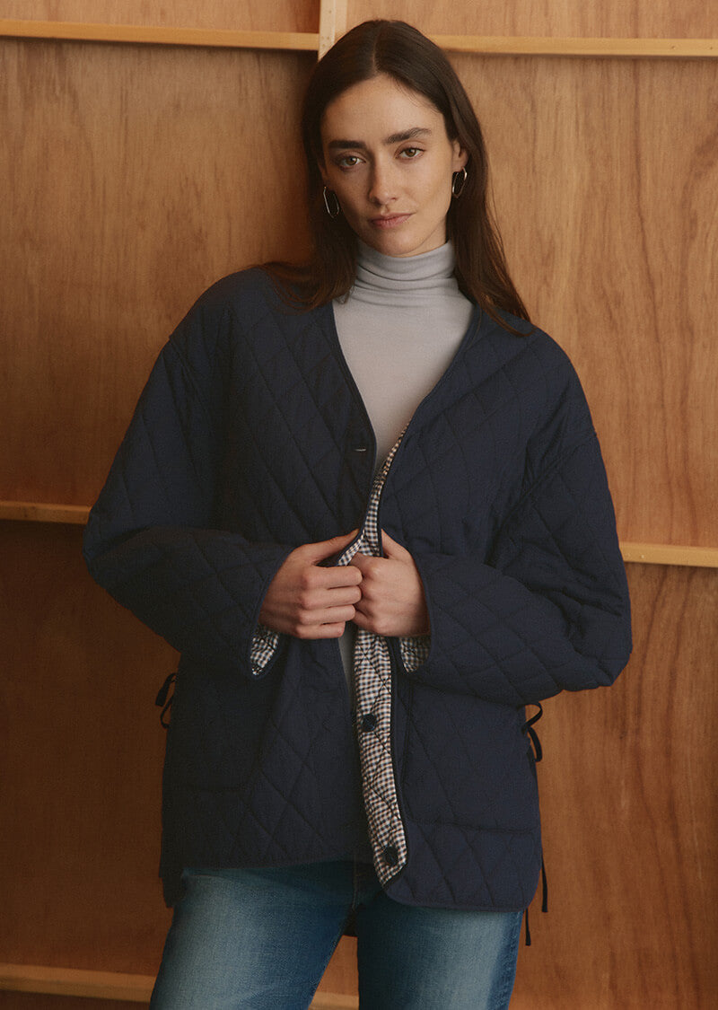 Woman wearing a navy quilted jacket over a gray turtleneck against a wooden background