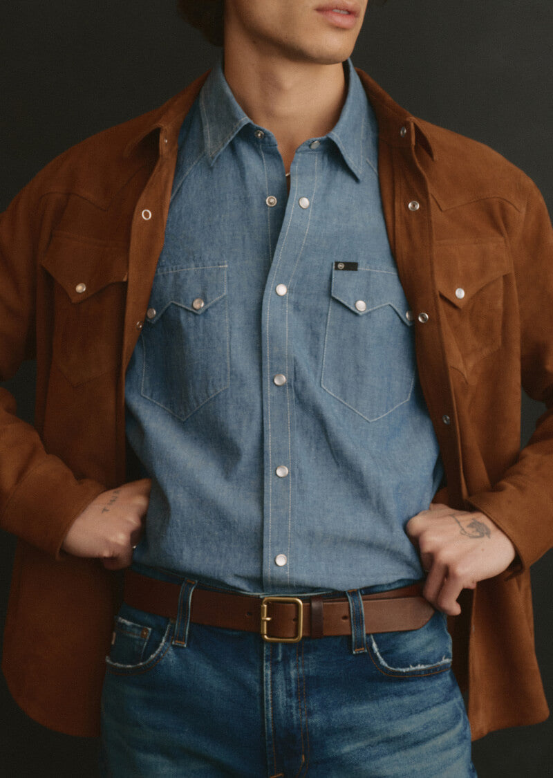 Person wearing a brown jacket over a blue denim shirt with a black background