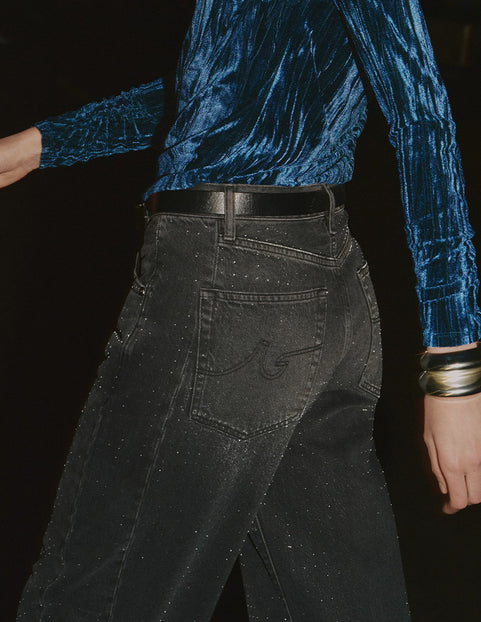 Person wearing a blue velvet top and black pants against a dark background