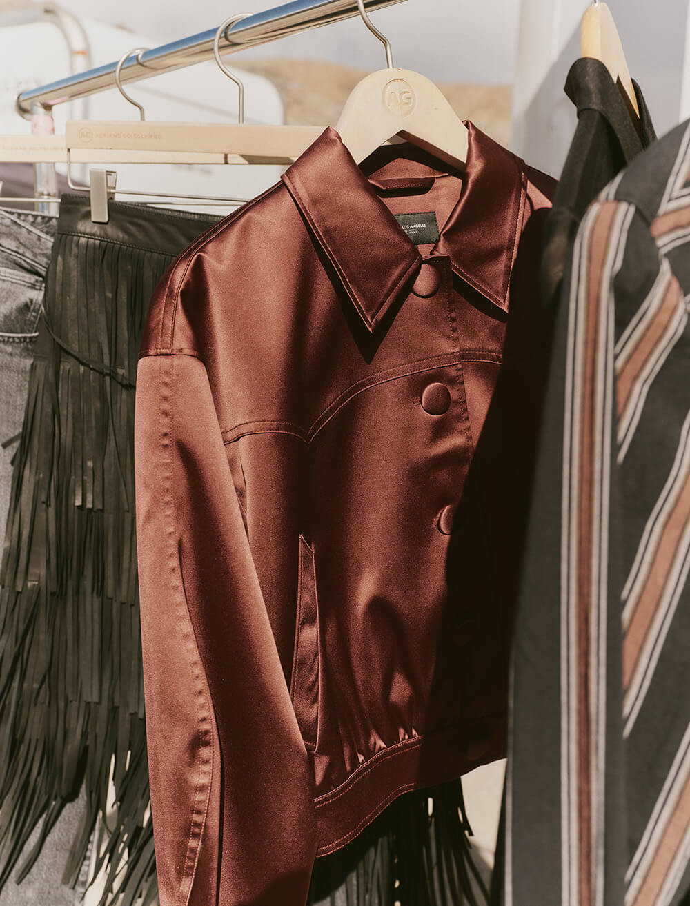Brown jacket hanging on a rack with other clothing items in the background