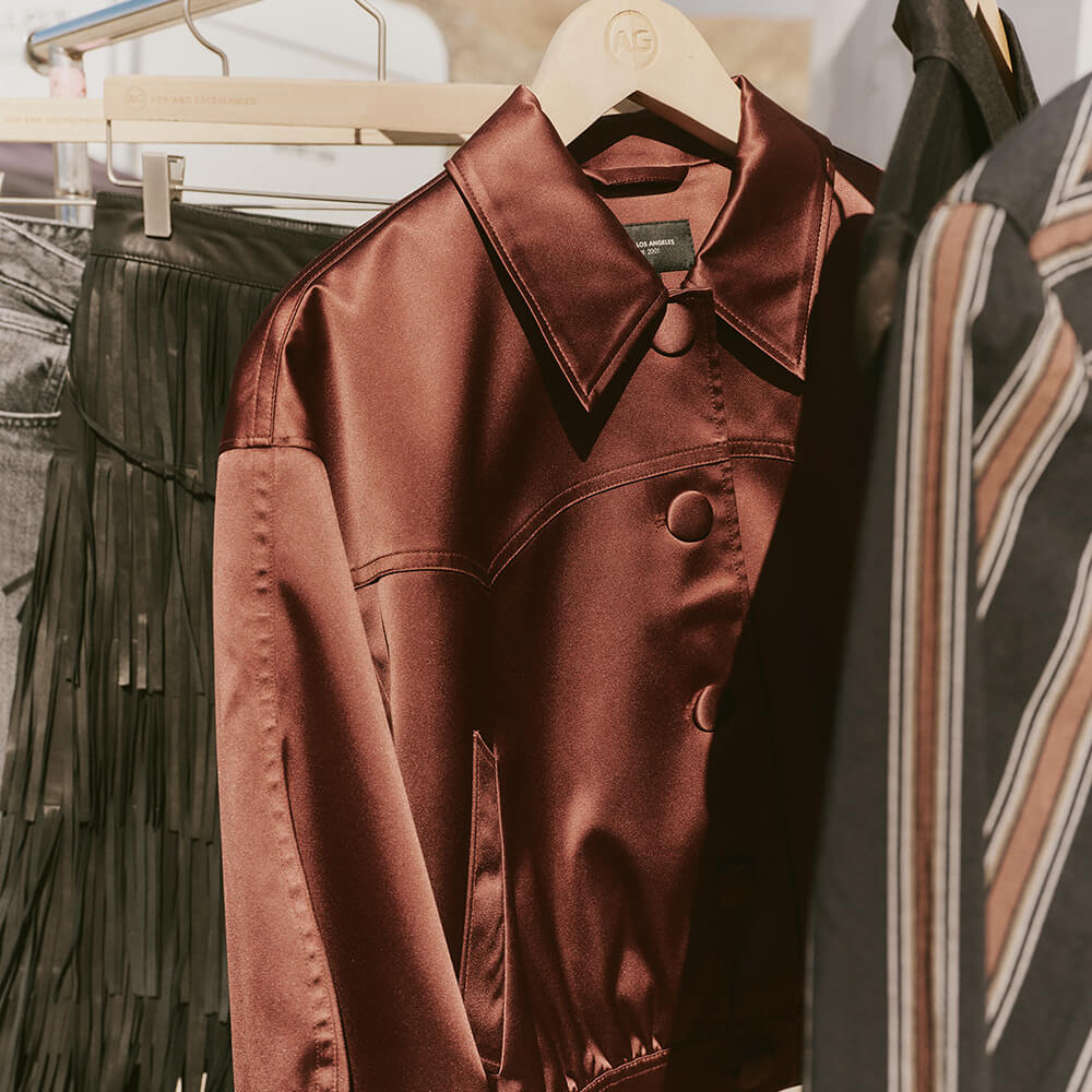 Brown satin jacket on a hanger with other clothing items in the background