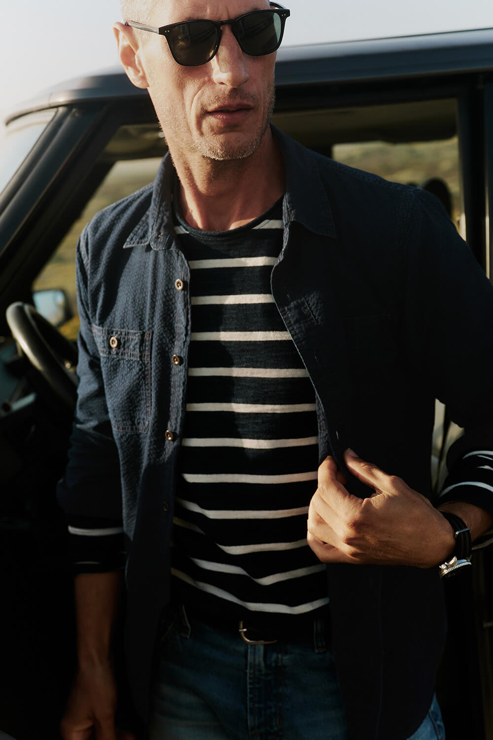 Man wearing sunglasses and a striped shirt standing next to a car.