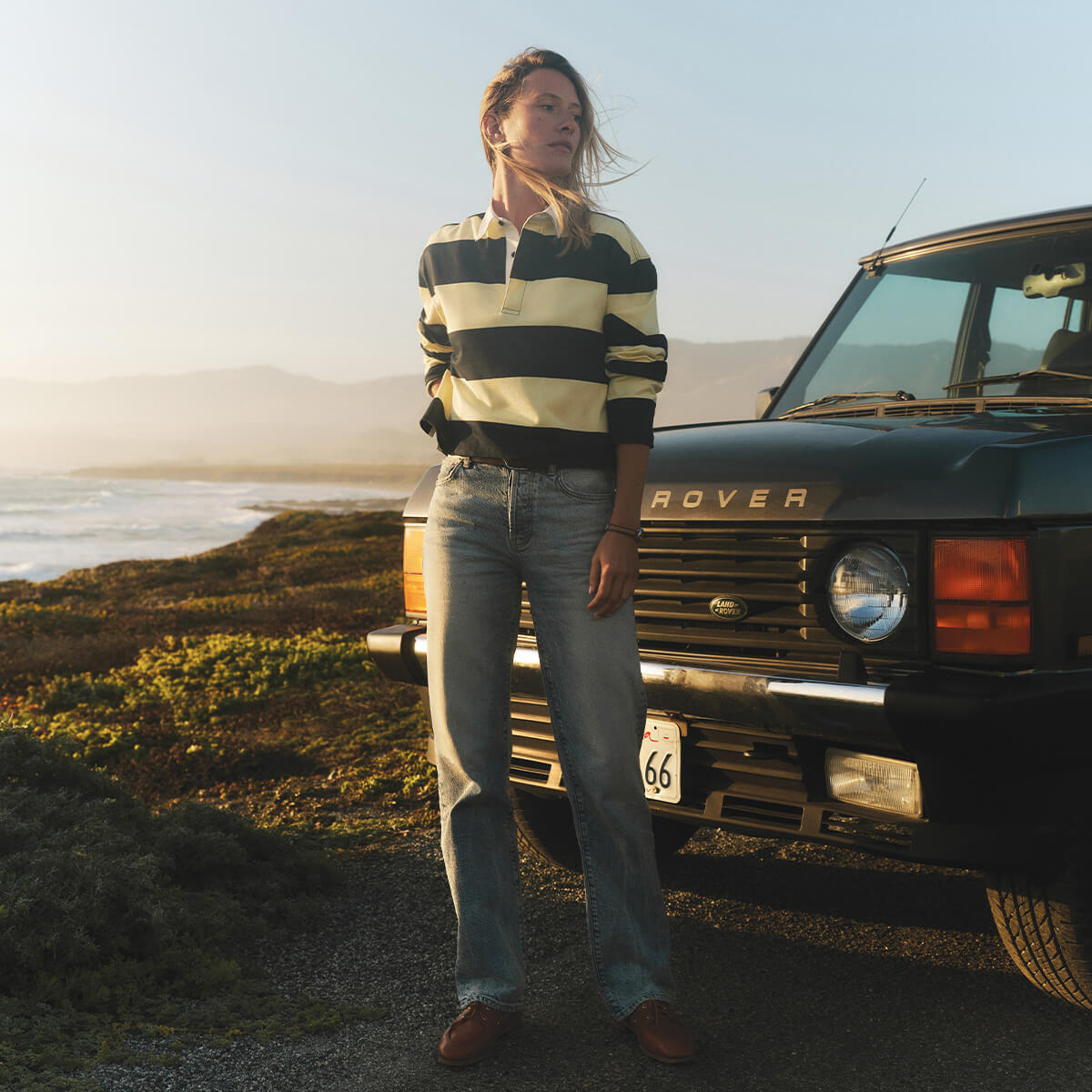 Person standing next to a black Land Rover on a scenic road.