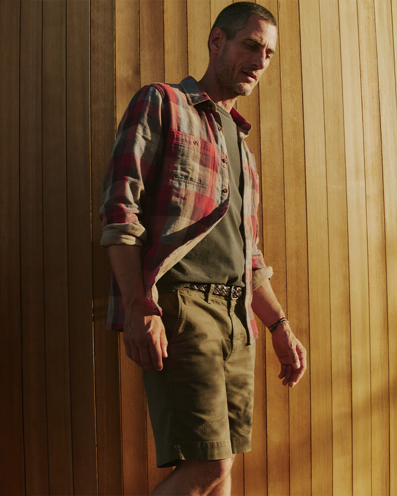 Man wearing a plaid shirt and shorts against a wooden paneled wall