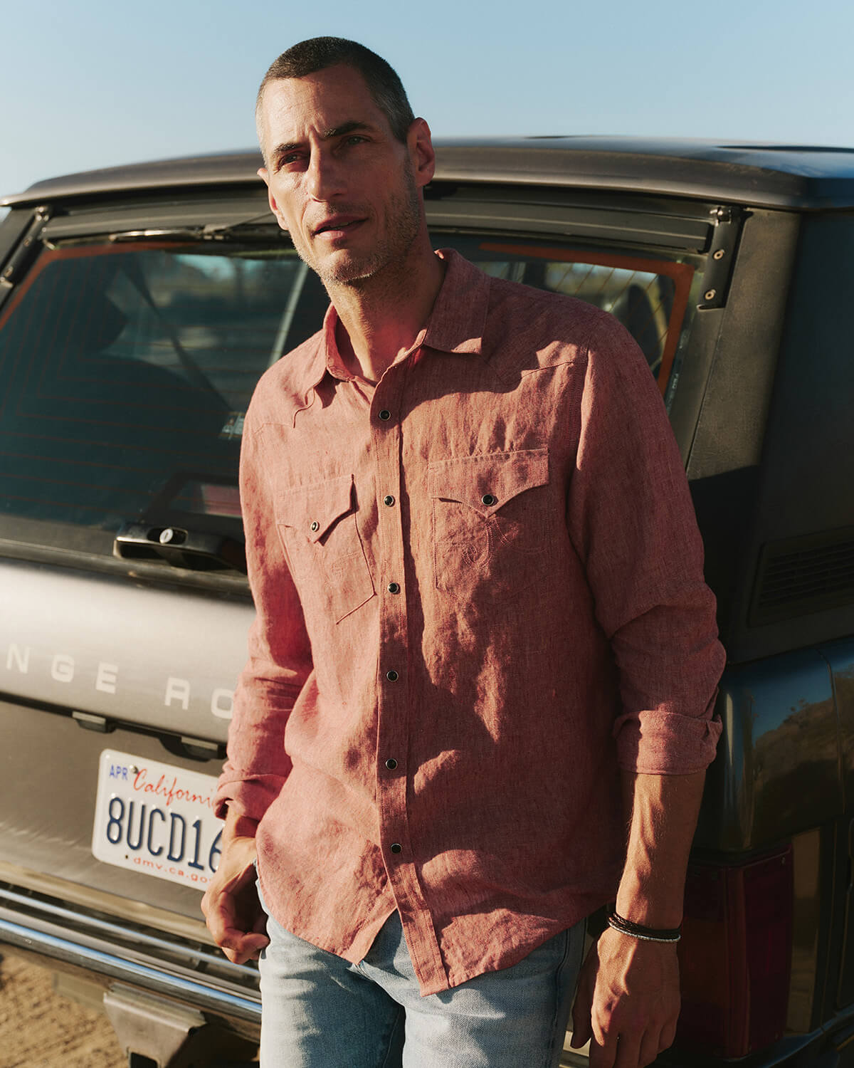 Man standing next to a vehicle wearing a pink shirt