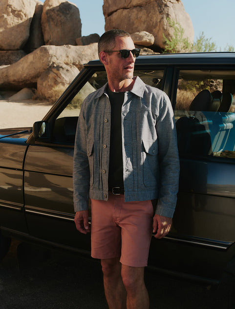 Man standing next to an open car door in a desert setting with large rocks and clear sky.