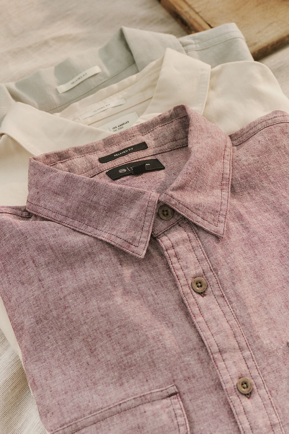 Close-up of a pink denim shirt with brand labels on a neutral background
