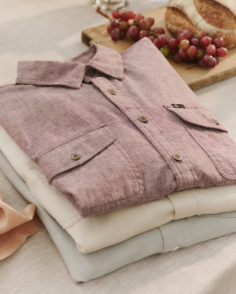 Folded pink corduroy shirt on a light surface with grapes in the background