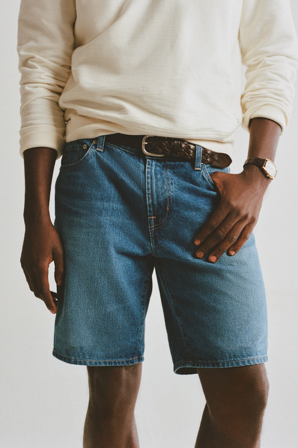 Person wearing blue denim shorts and a white long-sleeve shirt against a plain background