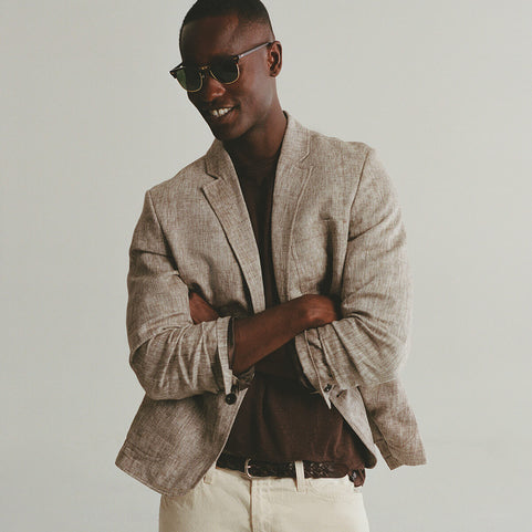 Man wearing a beige blazer and sunglasses against a plain background