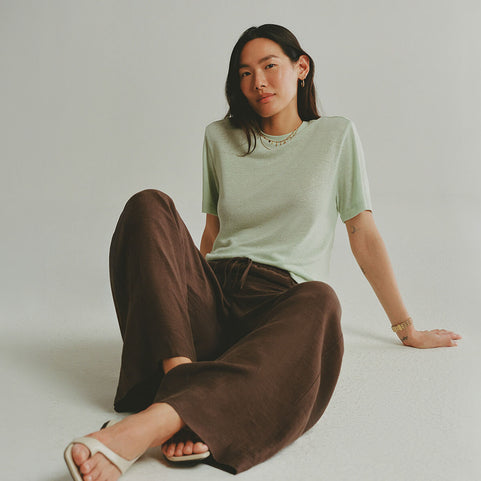 Person wearing a light green t-shirt and brown pants sitting on a white floor.