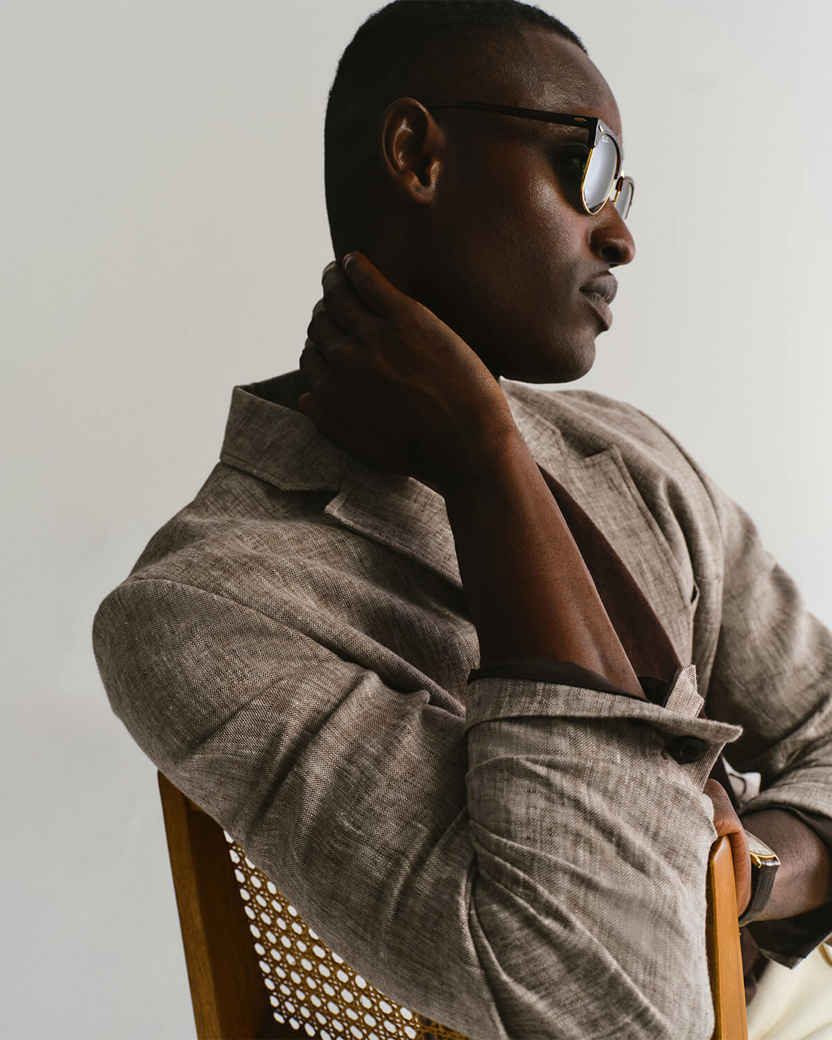 Person wearing sunglasses and a beige jacket sitting on a chair.