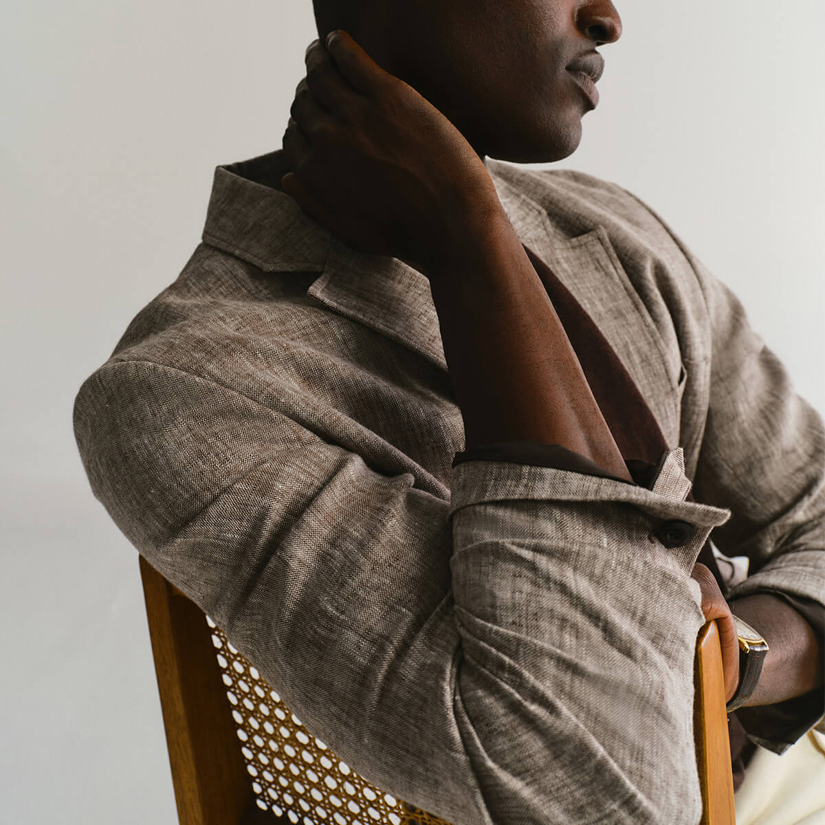 Person wearing a textured brown jacket sitting on a chair with a neutral background